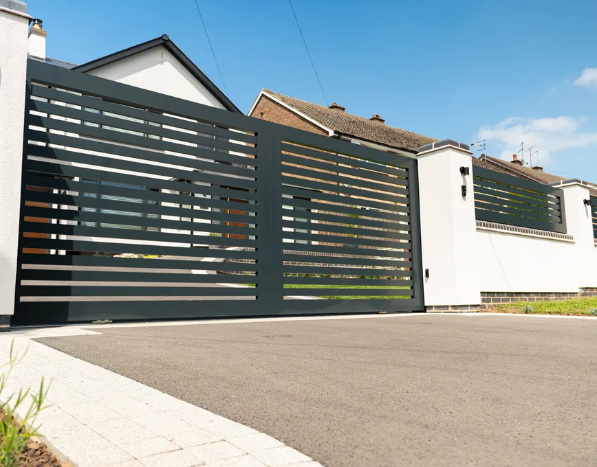 Anthracite aluminium sliding gate running along a rendered boundary wall, Cookhill