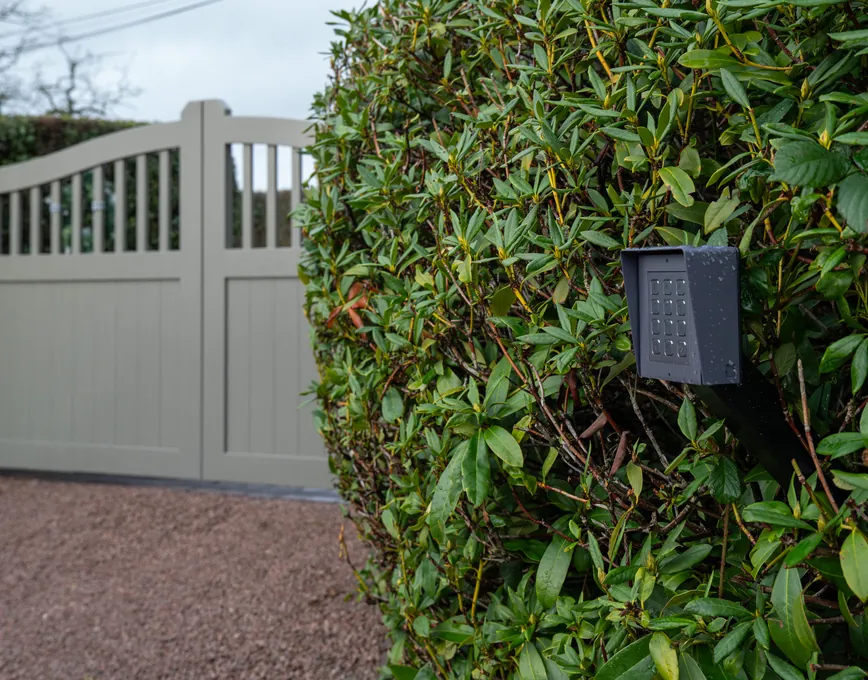 Warm grey traditional-style driveway gates with a curved spindle top and keypad