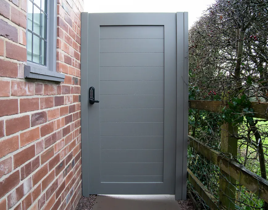 Modern warm grey panelled side gate beside a brick house