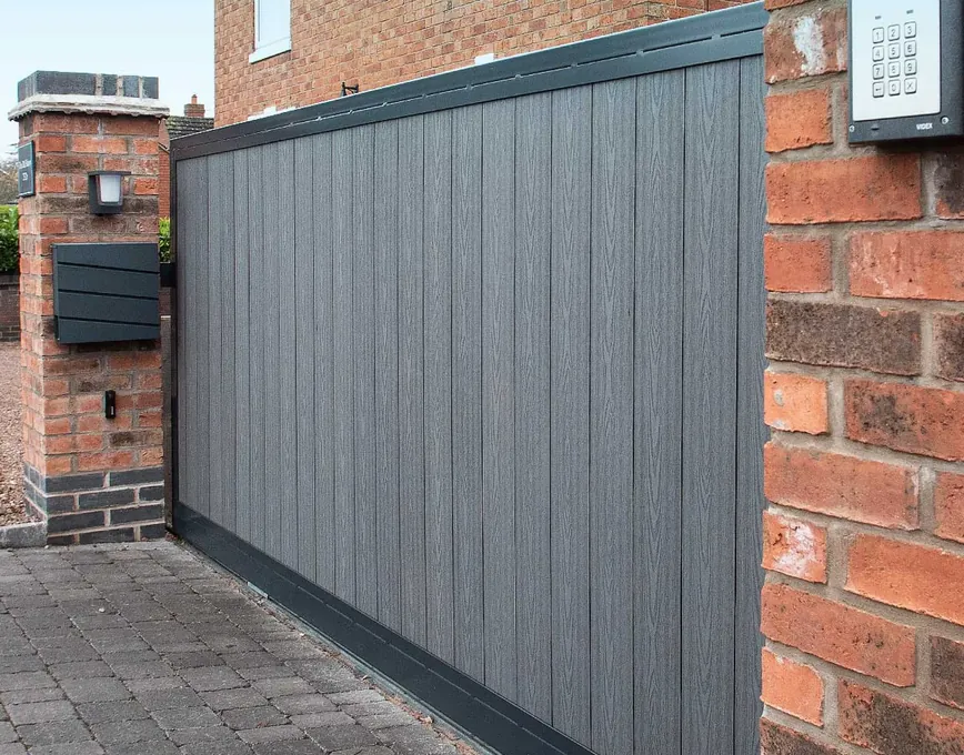 Grey composite sliding gate with keypad entry beside a brick pier