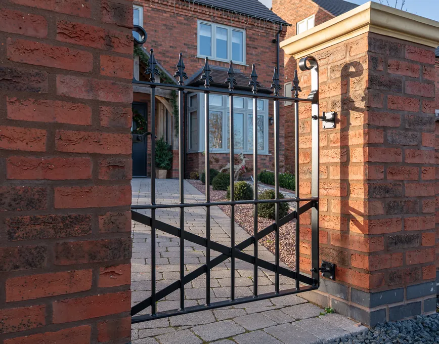 Black metal swing gate with spear-top railings between brick piers