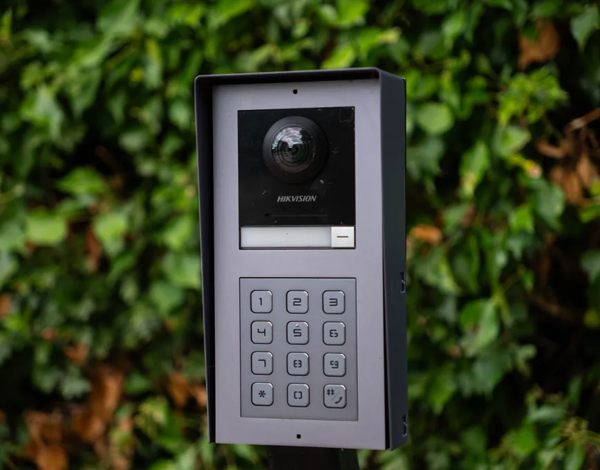 Video intercom with keypad beside a white estate-style gate