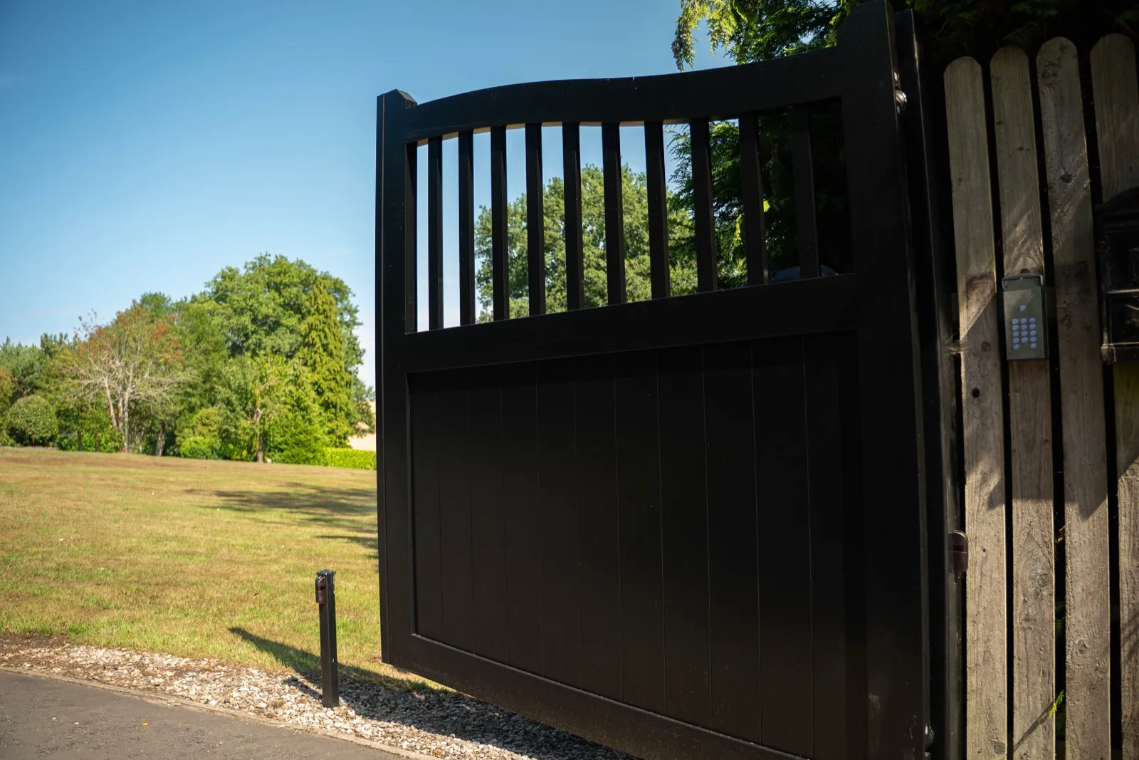 Black swing gate with a keypad on the post, opening onto a lawn