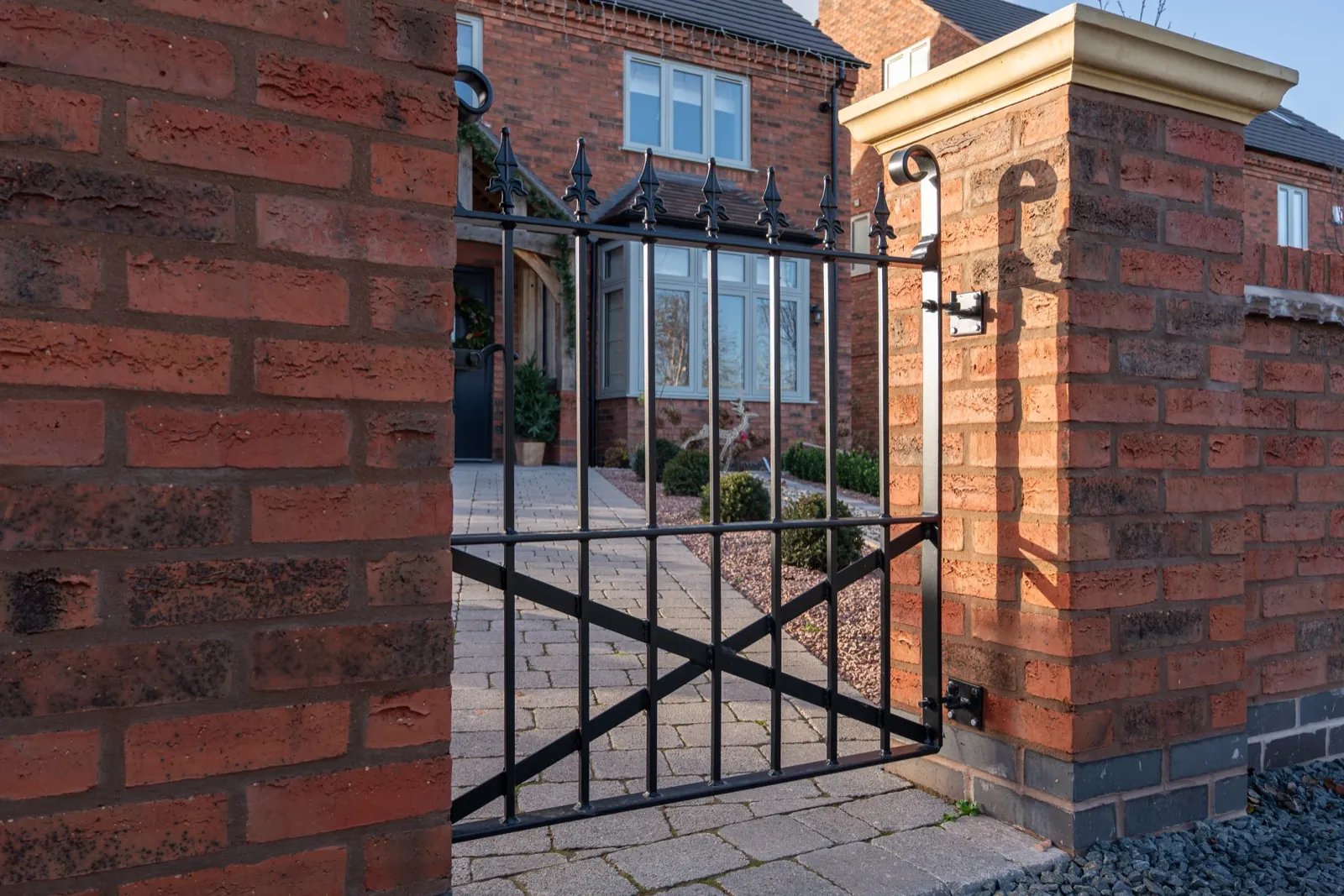 Black metal pedestrian gate with spear-top finials between brick piers