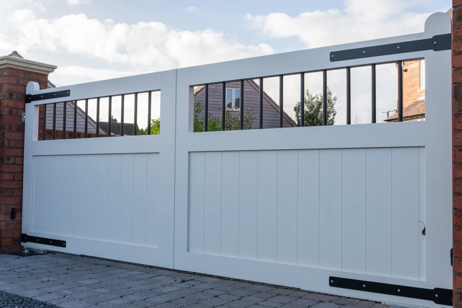Light grey swing driveway gates with black strap hinges and railed top