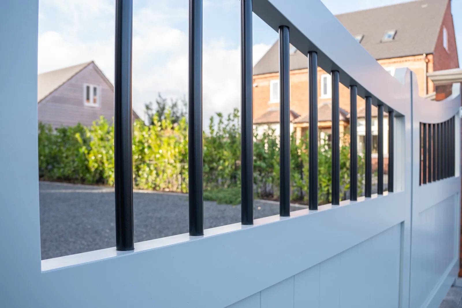 Close-up of black vertical rails set into the curved top of a light grey gate