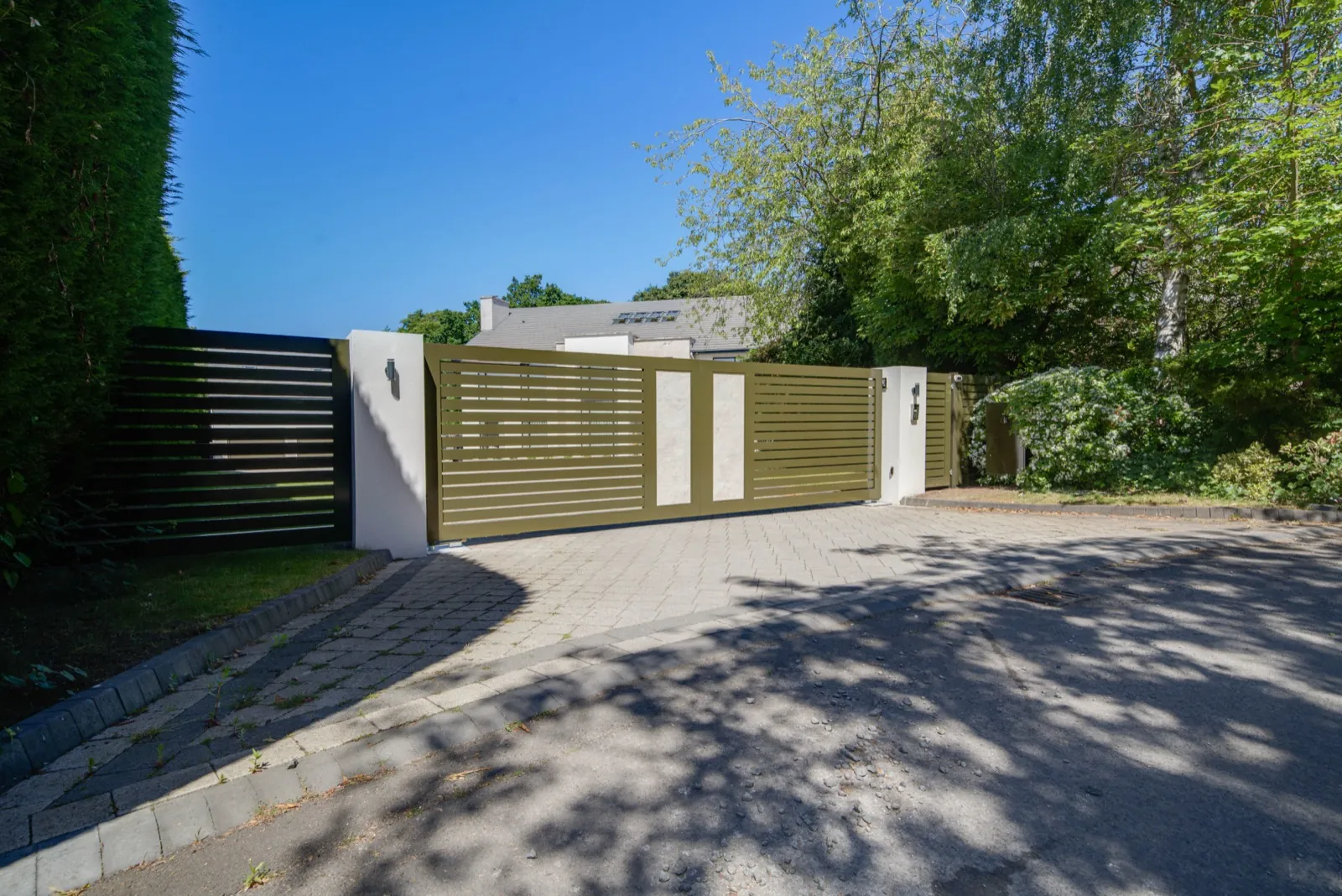 Olive green swing gates between white piers with a tall hedge