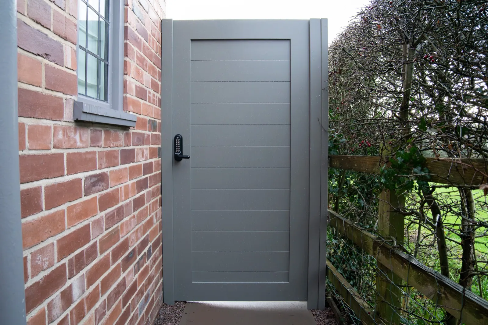 Solid warm grey side gate between a brick house and a hedge