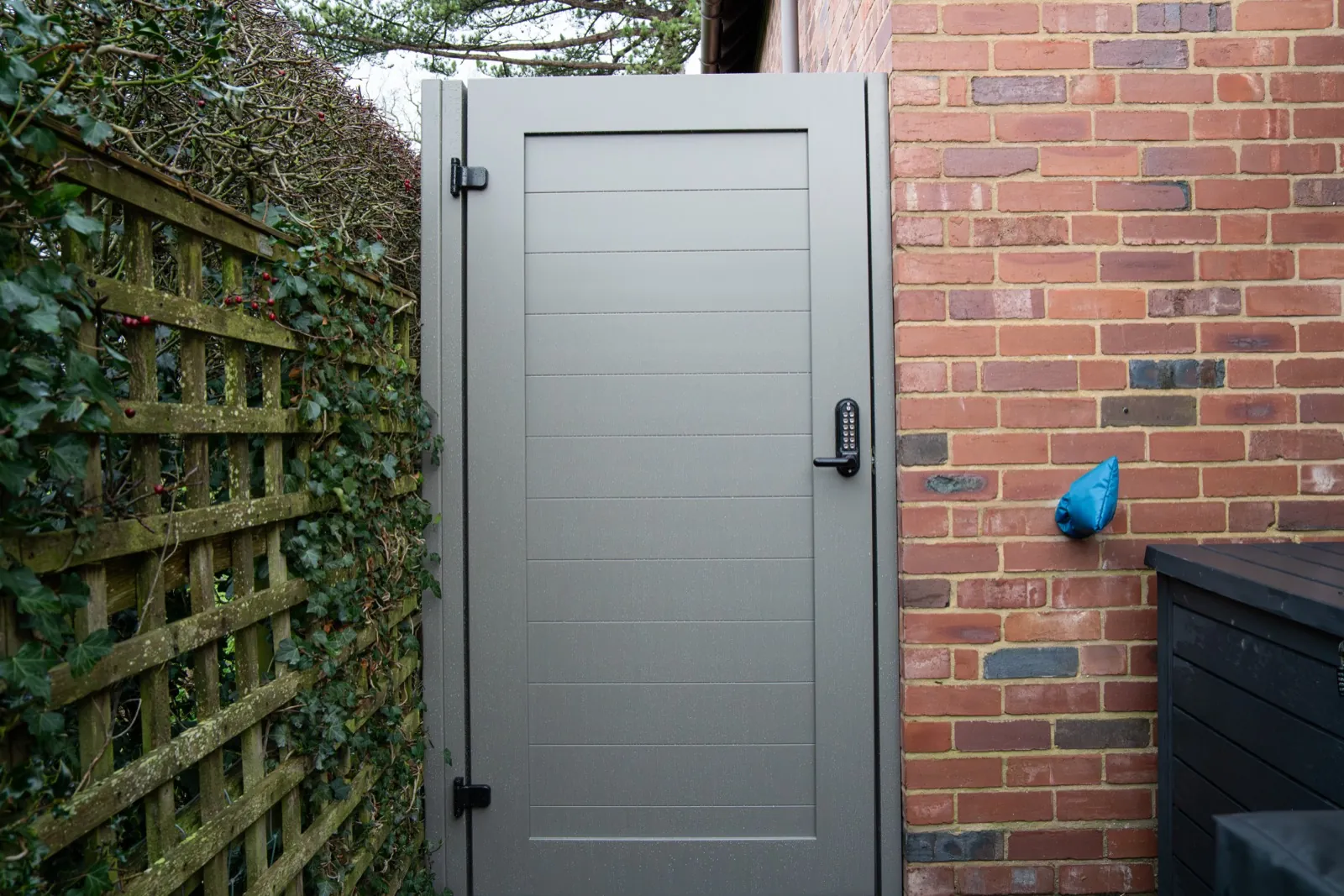 Warm grey side gate with a coded lock beside a brick wall