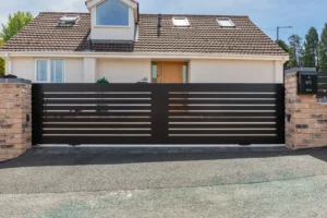 Black horizontal-slat sliding gate between brick piers in front of a house, Sutton Coldfield