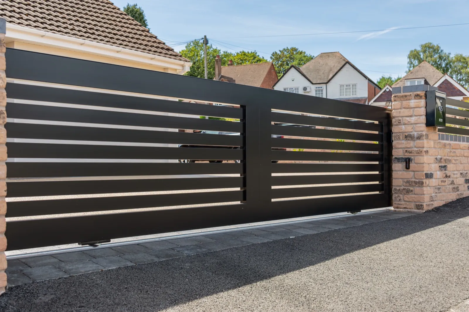 Black slatted sliding gate seen from an angle along the boundary