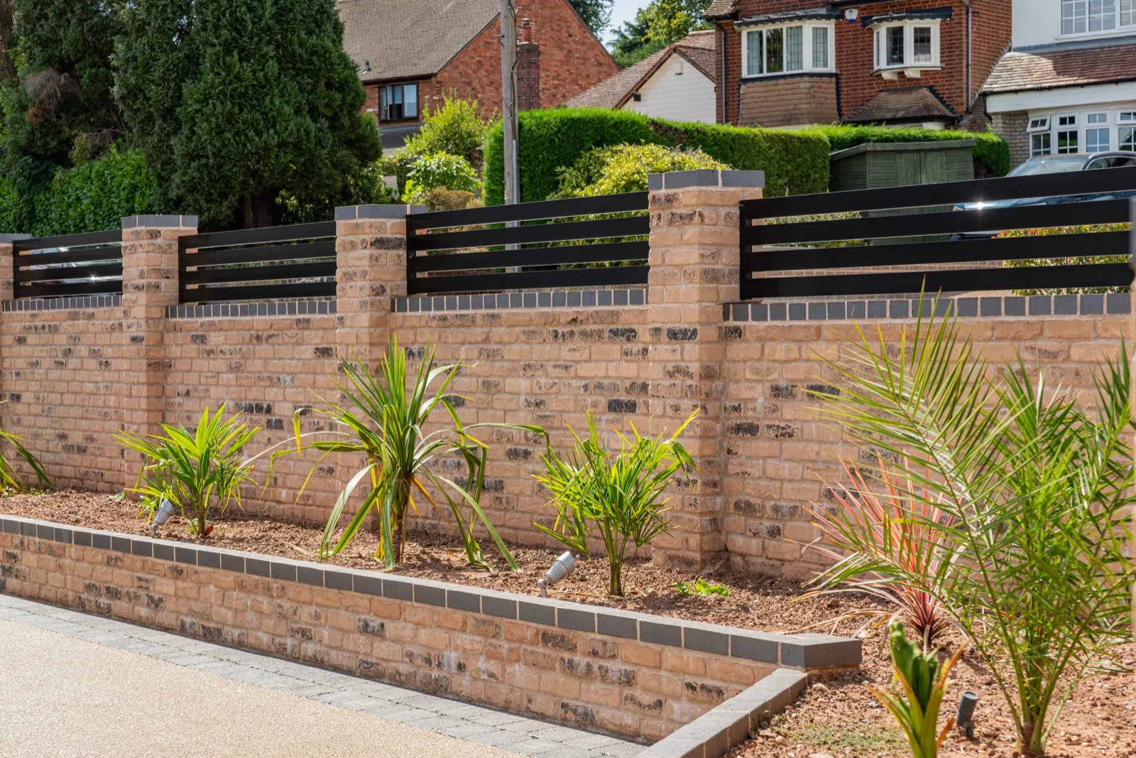 Black railing panels along a new brick boundary wall with planting