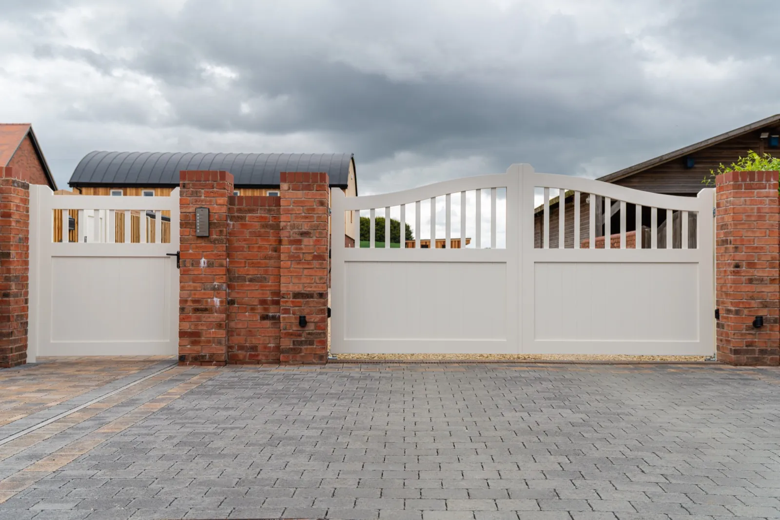 Cream driveway gates and matching pedestrian gate between brick piers