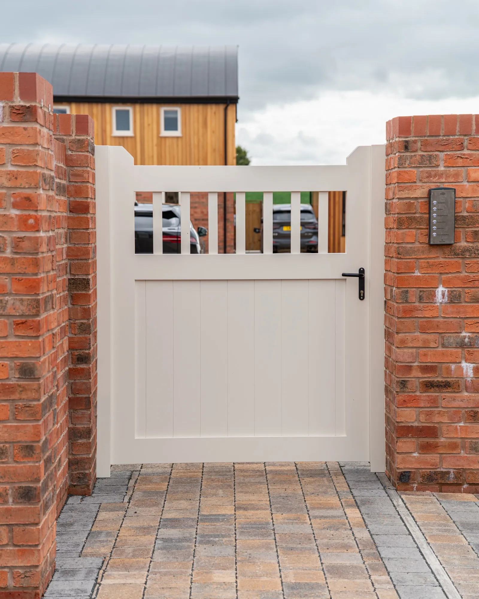 Cream pedestrian gate with a spindle top and keypad on the brick pier