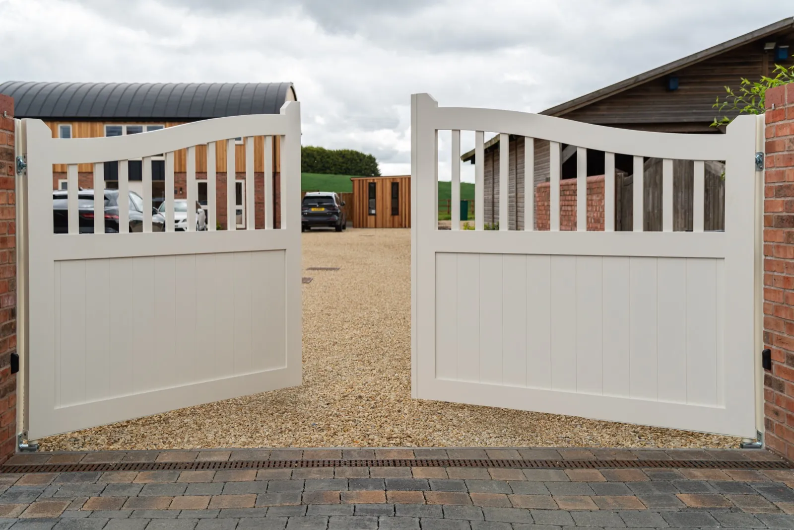 Cream automated swing gates standing open onto a gravel drive